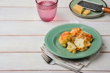 Cooked cauliflower grantin with bechamel sauce and cheese on a green ceramic plate on a light wooden background. Vegetarian recipes; side dishes.