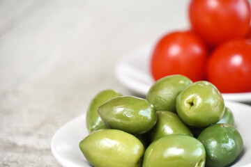 Close up plate of green olives and cherry tomatoes on white table with space for text. Mediterranean ingredients.