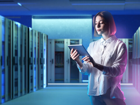 Woman system administrator. Girl is standing in server room. Data center system administrator. Woman with electronic tablet monitors load on servers. System administrator for hosting company