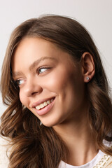 Fototapeta premium Beautiful young girl with fresh healthy skin. Woman advertise ear-rings. White background. Earrings closeup. Blond european woman with long hair with big lips, pretty smile. Cosmetology, scincare