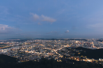 twilight city lights urban expanse evening sky skyscrapers aerial view cityscape illuminated streets mountainous silhouette dusk blue hour building density residential areas vibrant life roads lit up 