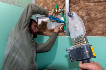 A mature bearded plumber cuts plastic pipes with special cutter and joins polypropylene pipe with...