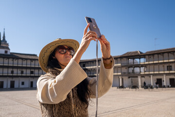 Middle aged female traveler with big rounded sunglasses and a cowboy hat taking picture of...