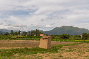 Obraz premium rural house in a green cultivated meadow, farm in a beautiful cultivated valley with mountains in the background