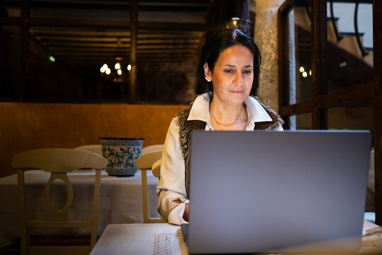 elegant and beautiful middle-aged woman teleworks with a laptop computer in a coffee shop.