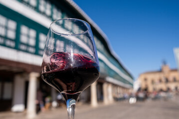 a glass of wine swirls to let the aromas come out and be tasted with the main square of Almagro in the background out of focus on a sunny day.