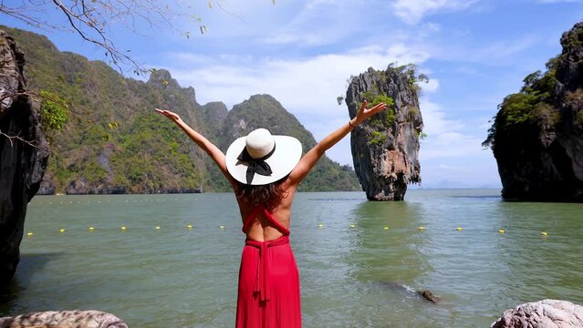 A tourist woman in a red dress looks at the famous sightseeing spot James Bond island at Phang Nga Bay, Phuket, Thailand