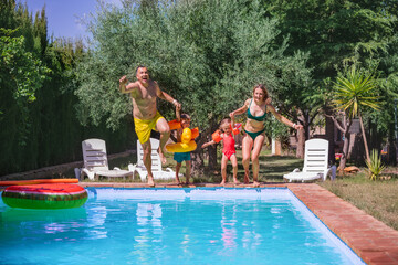 Happy family four in moment of jump into pool on sunny day