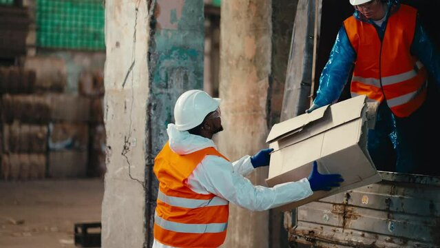 A man with Black skin in a white protective uniform in an orange vest accepts waste paper given to him by a brunette girl from a truck and stores it at the Large Waste Recycling and Sorting Plant