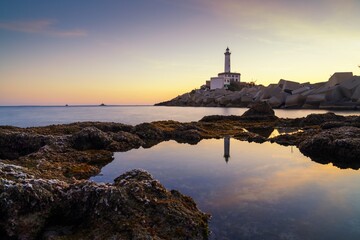 Naklejka premium landscape view of the Botafoc Lighthouse in Ibiza Town Port at sunsetwith reflections in tidal pools in the foreground