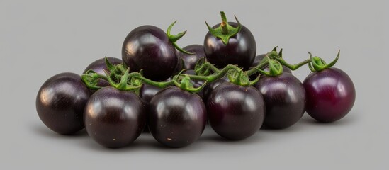 A group of black tomatoes, including Brads Atomic Grape heirloom cultivars of Solanum lycopersicum, are arranged on a plain gray background. The tomatoes vary in size, shape, and texture, creating a