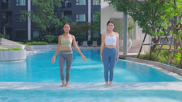 Young female friends are practicing yoga by the swimming pool in their condo.