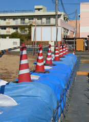 Fototapeta premium 乾燥中のコンクリート基礎と平行に並べられたパイロン。 赤パイロンとブルーシートによる立ち入り禁止警告。 日本の工事現場の風景。