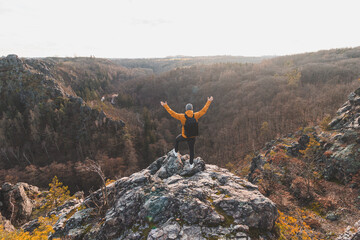 Traveller in a yellow jacket standing on the edge of a rock enjoying a moment of relaxation and a view of the Divoke sarky valley, Prague, Czech Republic. Achieving success