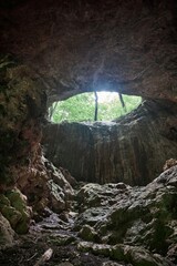 Large vertical cave, entrance from above, mountain landscape