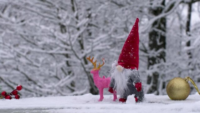 Close-up of New Year's toys in the snow. New Year is approaching. Red rowan, gnome, deer and golden ball on white snow.