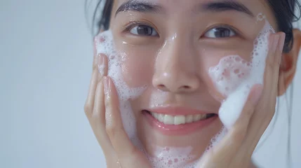 Fotobehang A cute asian girl have natural face with clean skin washes with a little foam cleanser and little water on her face in white background © sambath