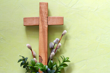 Wooden cross with boxwood twigs and catkins on green background. Palm Sunday concept