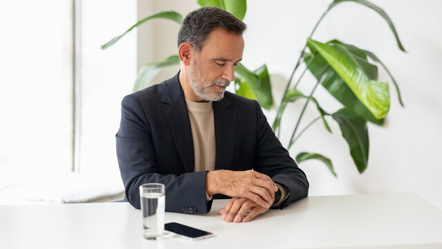 Contemplative mature businessman sitting at a white table with his smartphone