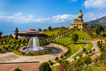 A statue of the Lord Buddha located on the top of the mountain surrounded by a beautiful green garden with fountain.  A beautiful Cloudscape in a clear blue sky adds a mesmerizing effect to the scene.