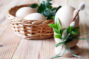 Egg in egg cup decorated catkins and boxwood and eggs in basket on wooden background, easter concept 