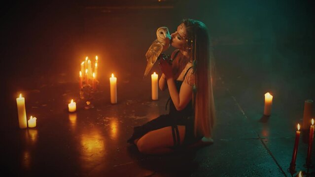 fantasy gothic woman sitting on knees floor magic ritual circle of candles, lady holding white barn owl bird kissing wings Elf sexy girl hug embrace little birds. fashion model dark room black dress