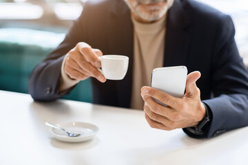Close-up of a man's hands as he multitasks with a white espresso cup in one hand