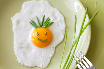 Funny fried egg with smiling smiley on plate with chives, creative breakfast concept