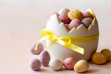 Colored chocolate easter eggs candy in eggshell shaped bowl on pink background, easter sweets, decoration
