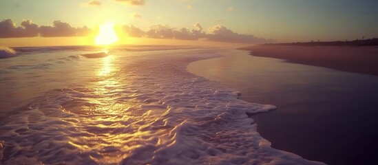The sun is setting, casting orange hues across the sky and reflecting beautifully on the calm ocean waters at the beach.
