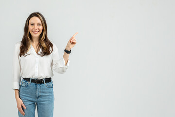 Radiant young woman in a white blouse and blue jeans standing with one hand on hip
