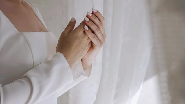 A young beautiful girl strokes her hands standing in front of a bright window. Close-up hand shots