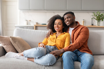 Black young millennial couple find relaxation on couch embracing indoor