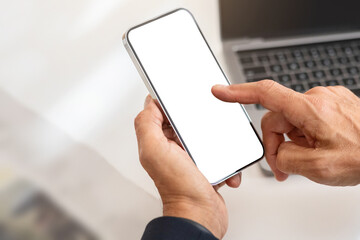 Close-up of a man's hands using a smartphone with a blank screen, with the keyboard of a laptop