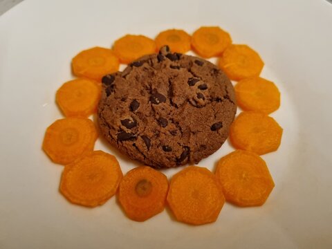 Delicious chocolate chip cookie surrounded by thin carrot slices on a white plate