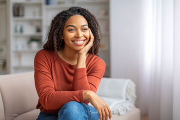 Beautiful young black woman sitting comfortably on couch in living room