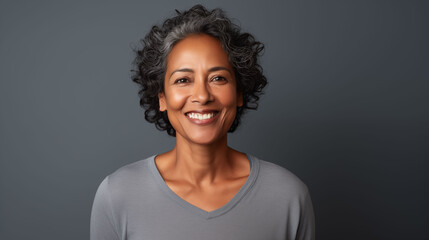 Close up of  mature woman with brown skin, grey short hair, wavy hair and a clear grey t shirt, isolated in a light grey studio. Portrait person. - obrazy, fototapety, plakaty
