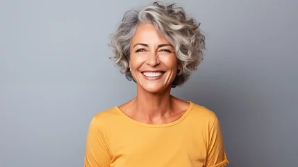 Fotobehang Close up of  mature woman with white skin, grey short hair, wavy hair and a clear yellow t shirt, isolated in a light grey studio. Portrait person. © Sittipol 