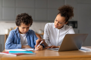 Concerned black mother assisting focused son with difficult homework