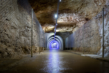 Stone tunnel drilled underground in the rock with blue illuminations and protective fence, exit...