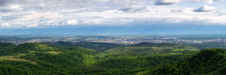 Kutaisi cityscape panorama seen from Sataplia Nature Reserve with Former Georgian Parliament Building and green hills and Colchis forests around, summer, Georgia.