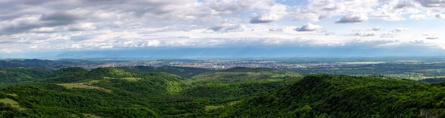 Kutaisi cityscape panorama seen from Sataplia Nature Reserve with Former Georgian Parliament Building and green hills and Colchis forests around, summer, Georgia.