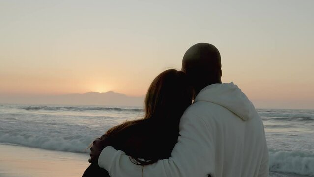 Rear view of casually dressed loving young couple watching beautiful sunrise morning over beach and sea in South Africa with lens flare - shot in slow motion