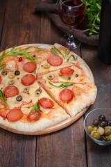 Homemade pizza with pepperoni, cheese and herbs on a dark wooden background