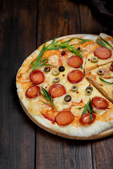 Homemade pizza with pepperoni, cheese and herbs on a dark wooden background