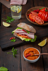 Sandwich with pulled ham, green salad and tomatoes on dark wooden background