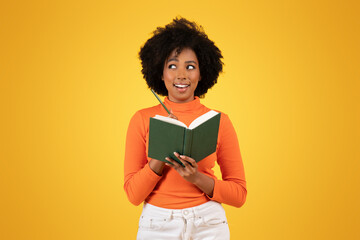 Inquisitive young woman with afro hair, in orange turtleneck, pensively holding a green book
