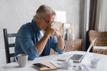 Frustrated middle-aged man massaging his nose and keeping eyes closed while sitting at his working...