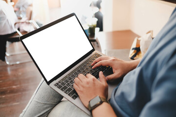 Mockup image of laptop computer. A man sitting cross legged with laptop computer with blank white screen at coffee cup, over shoulder view