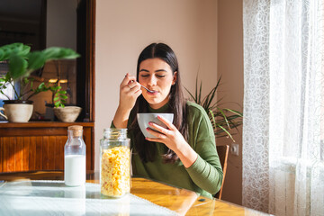 A young woman eating corn flakes for breakfast in the morning in her apartment	